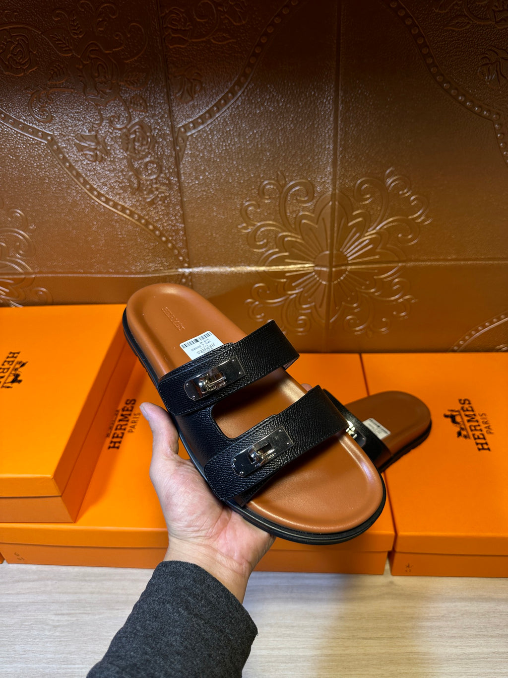 Dark slide sandals held in hand; double straps with metal buckle at top