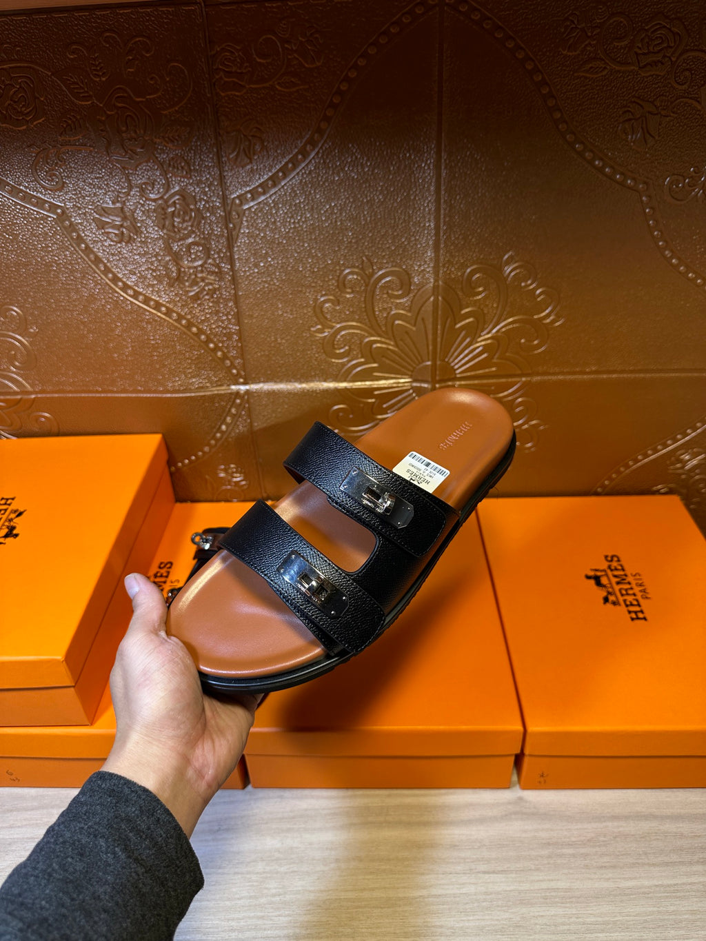 Dark slide sandals held above box; two straps with buckle hardware