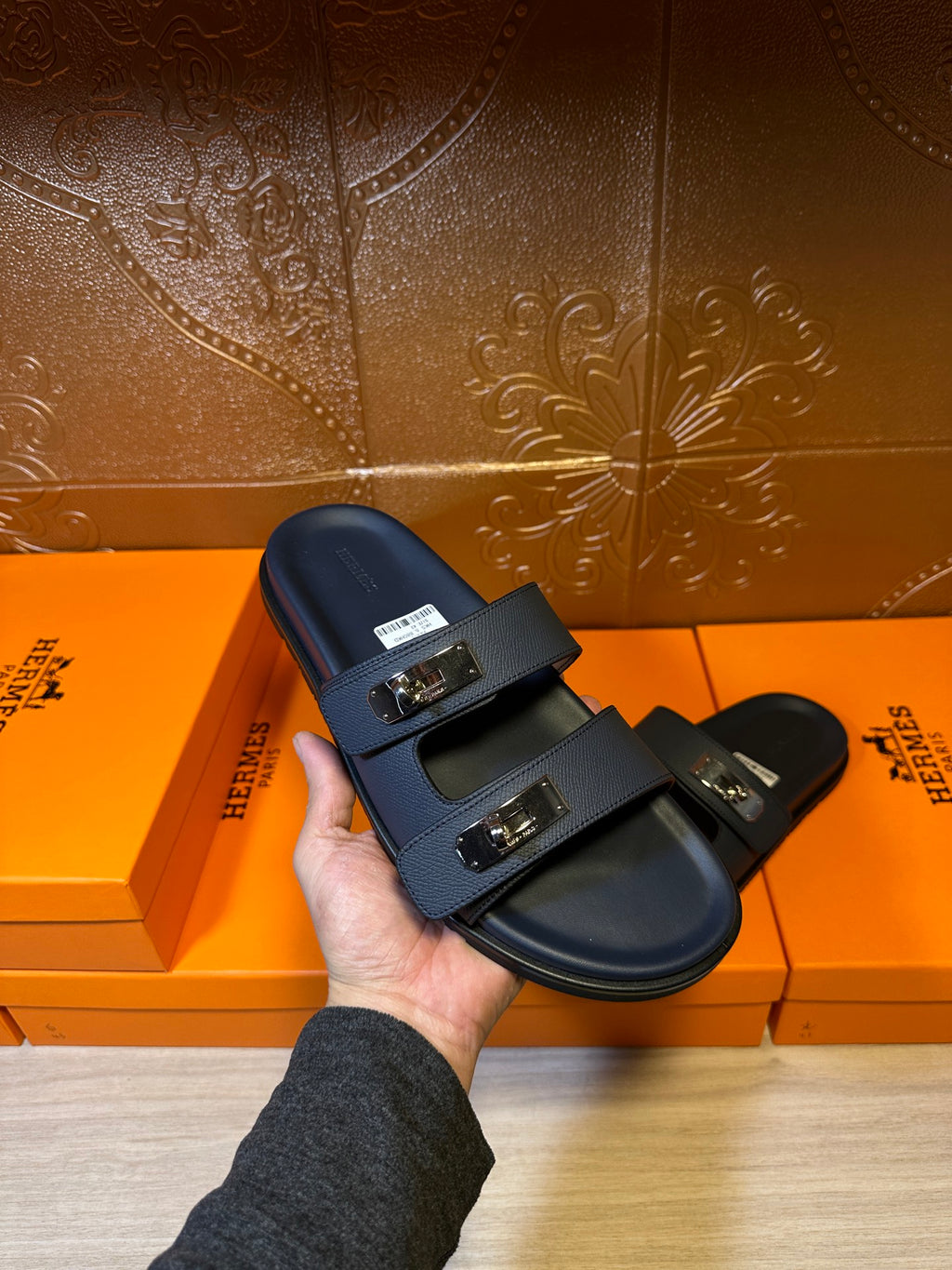 Blue leather slide sandals with two straps and metal buckles held in hand