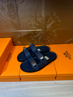 Blue leather slide sandals with two buckle straps, angled view on display box