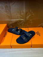 Blue leather slide sandals with double straps and metal buckles, angled pair