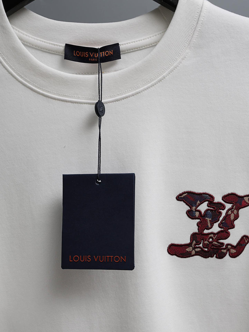White T-shirt collar with hanging brand tag and burgundy embroidered chest motif
