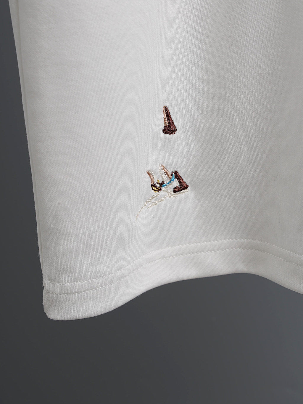 White T-shirt corner with small embroidered bird graphic near the hem