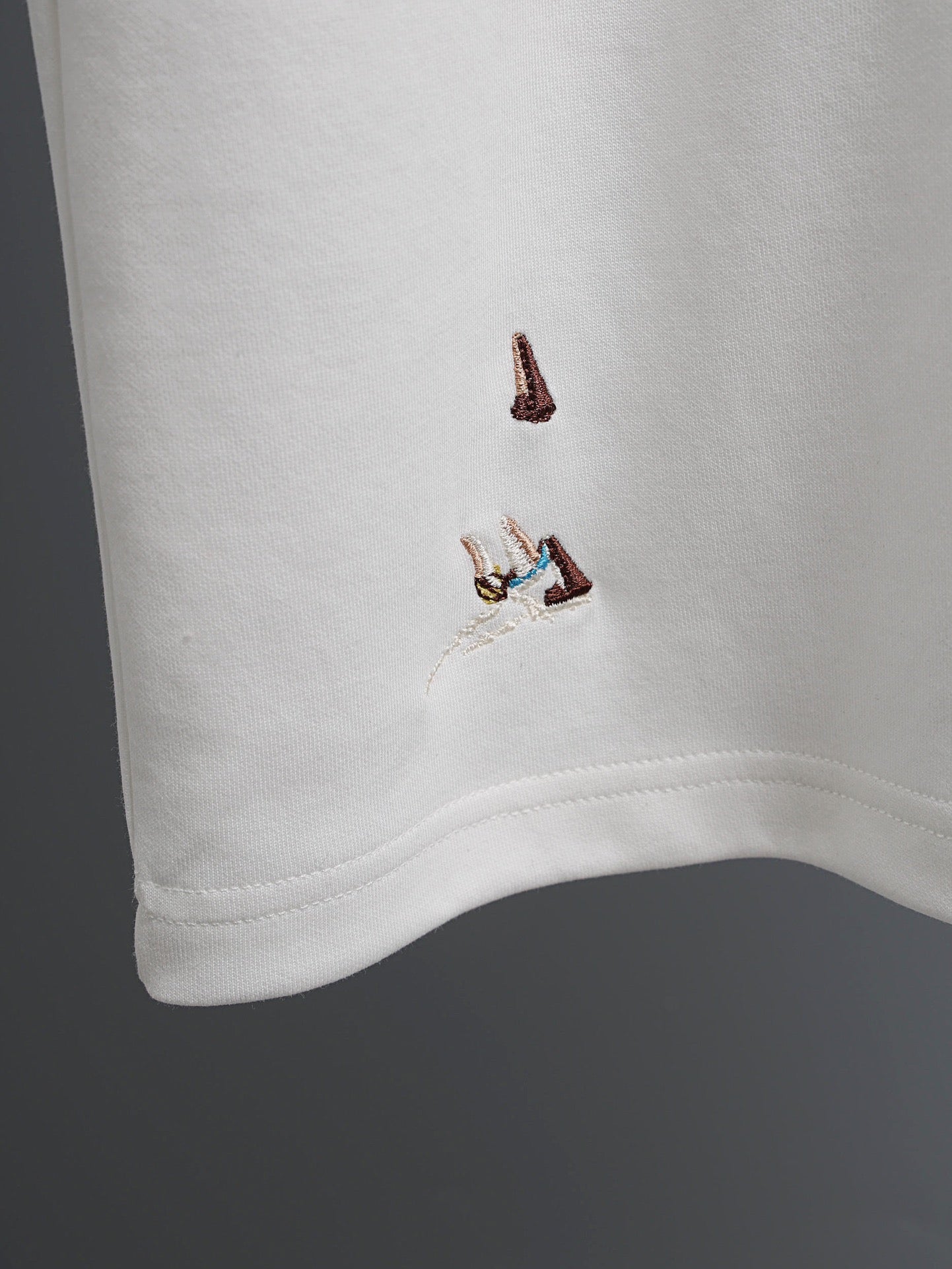 White T-shirt corner with small embroidered bird graphic near the hem