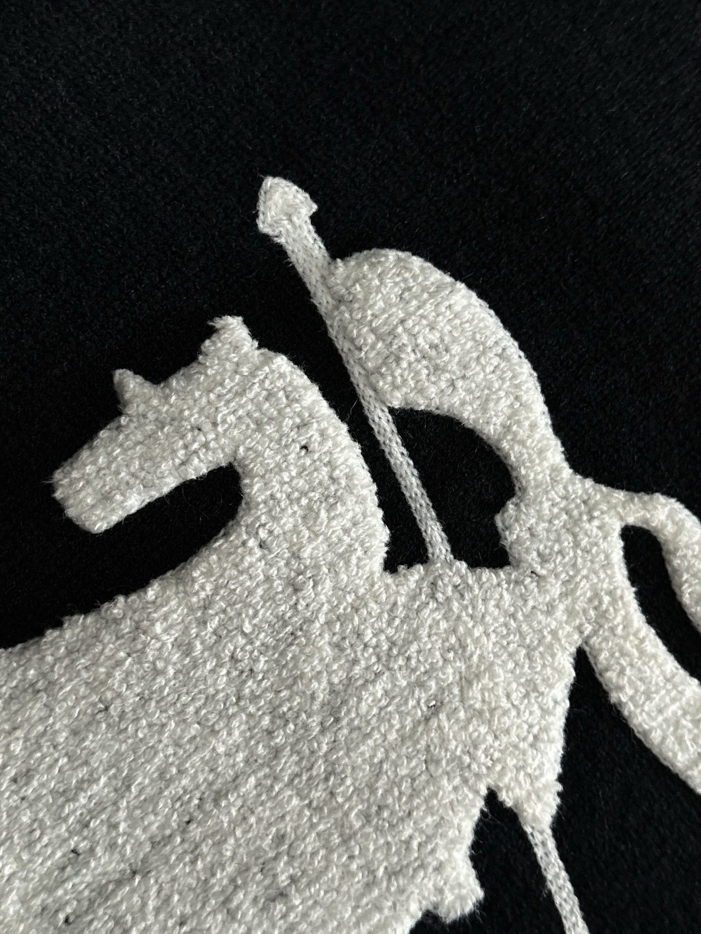 Black knit sweater close-up of white embroidered horse graphic
