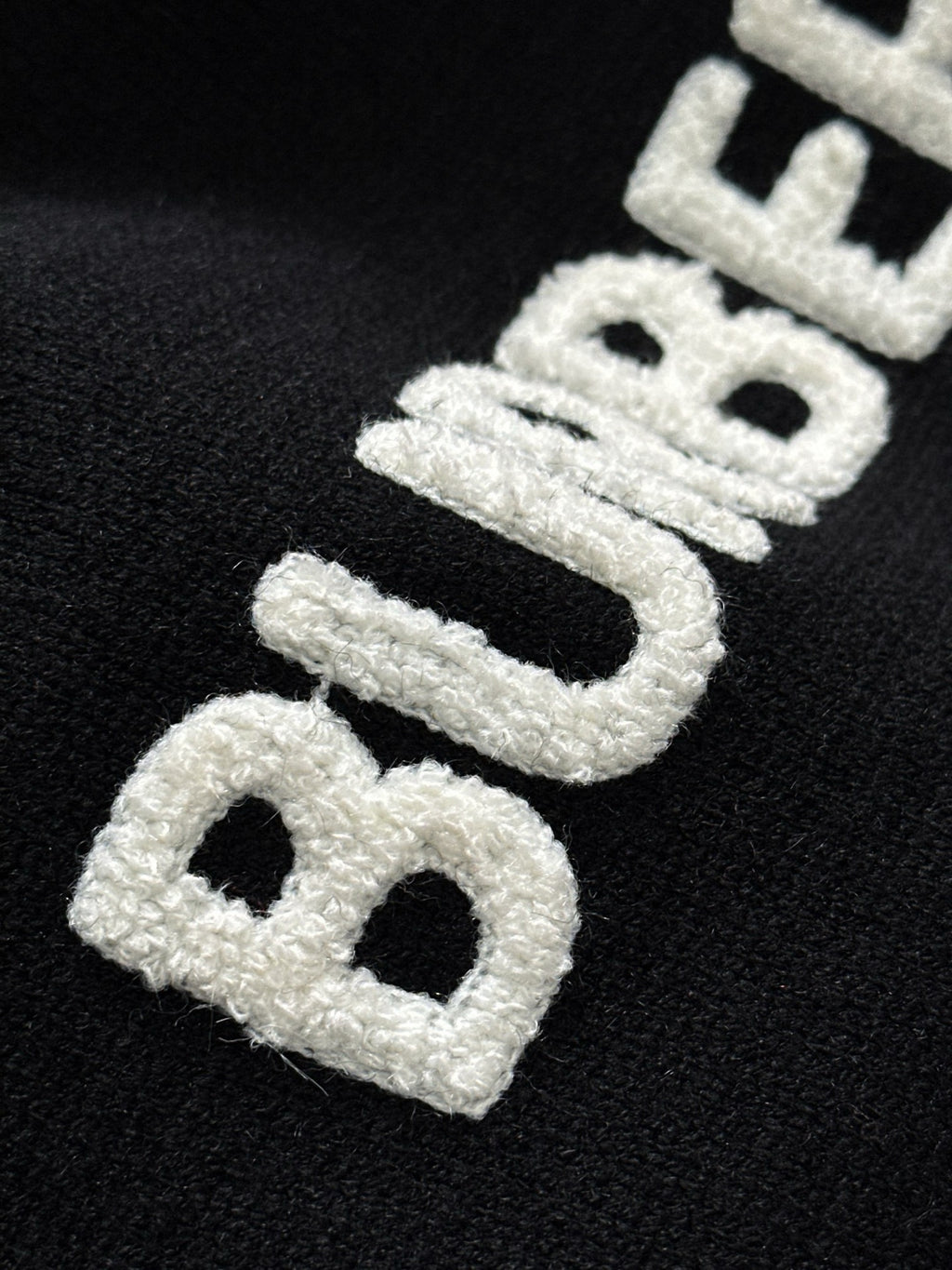 Black knit sweater close-up of large white embroidered “BURBERRY” letters