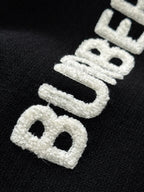 Black knit sweater close-up of large white embroidered “BURBERRY” letters