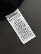 White fabric care label with BURBERRY text on black knit sweater