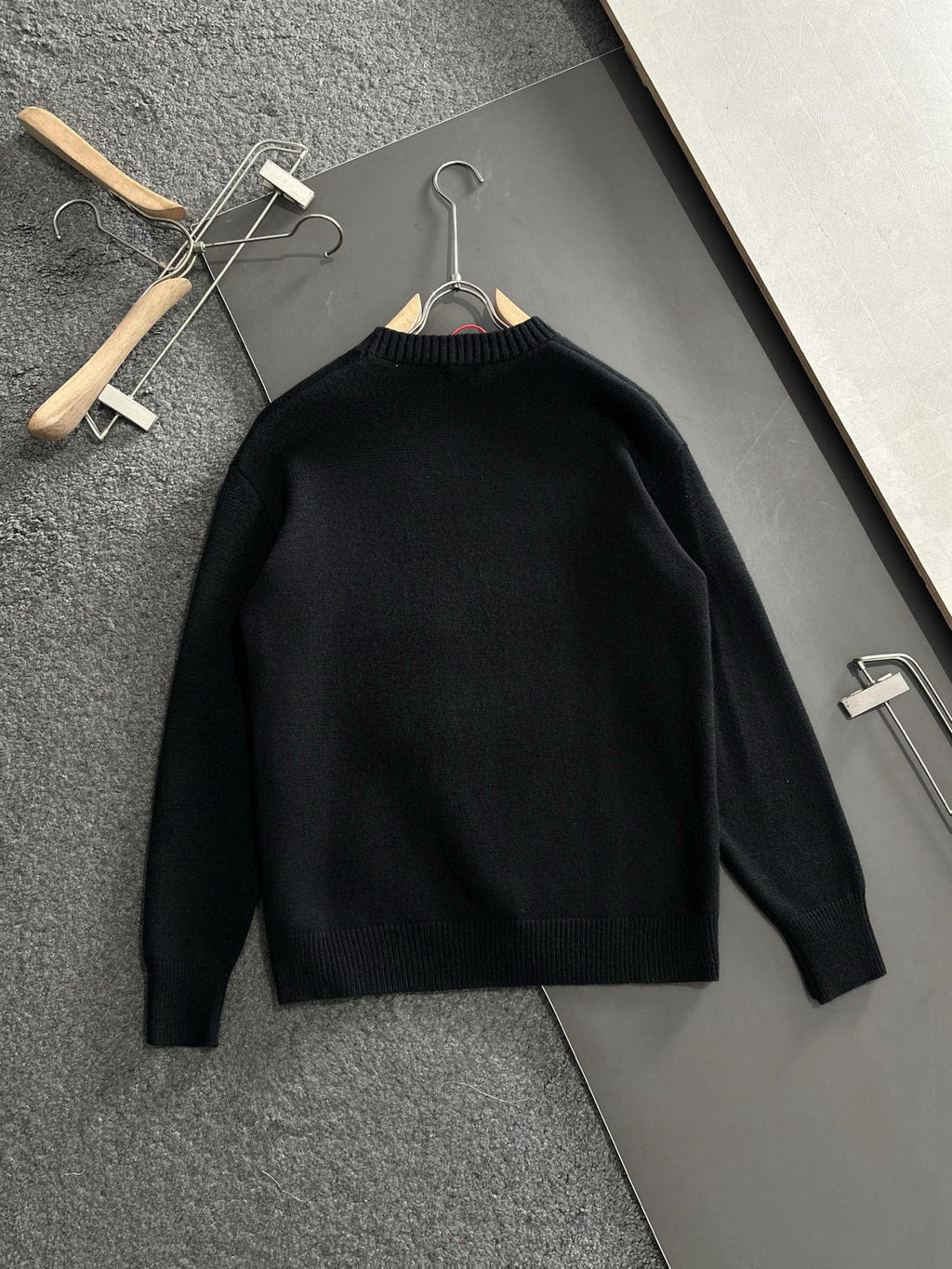 Black knit sweater hanging on wooden hangers, plain front with crew neckline