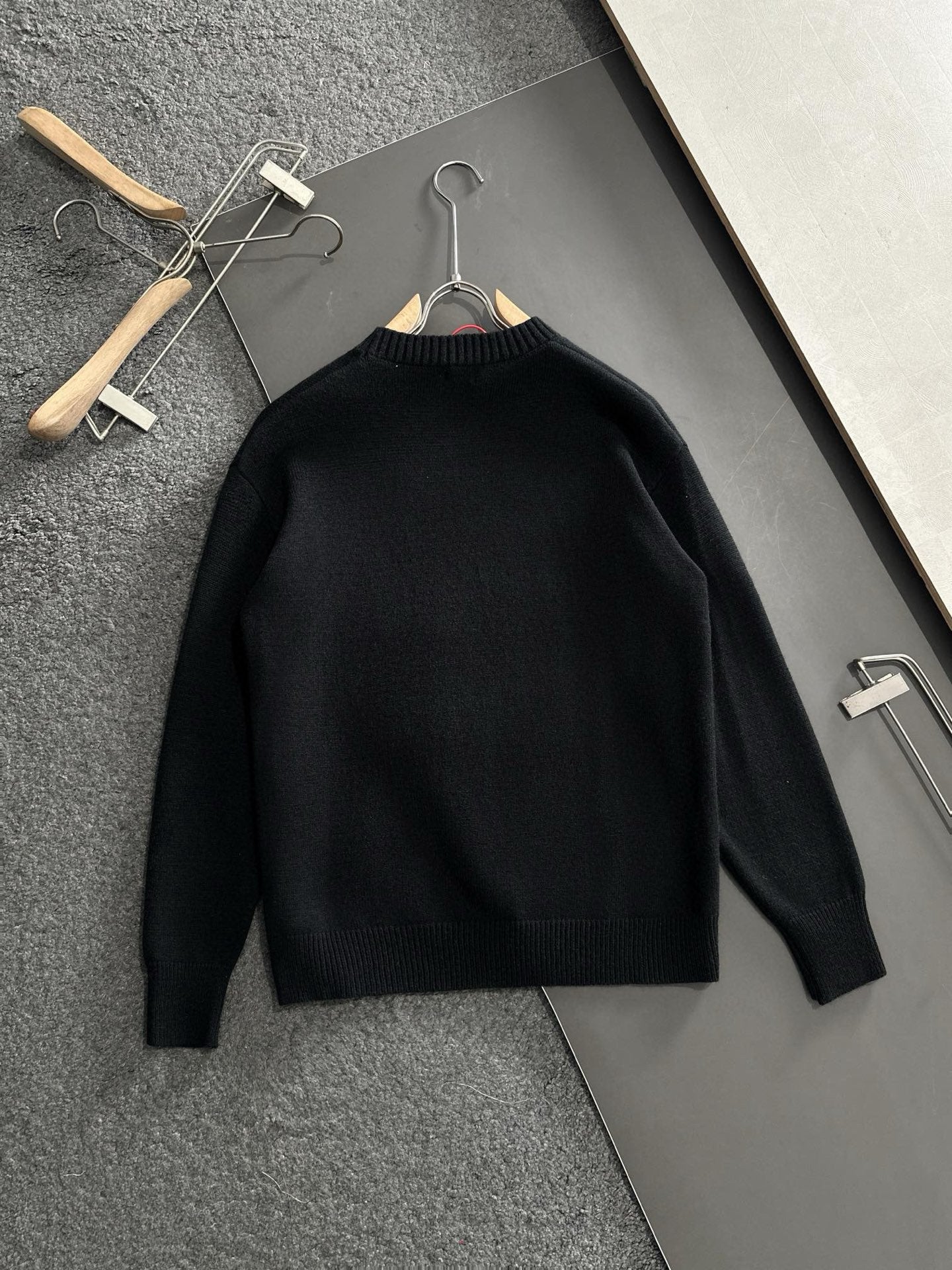 Black knit sweater hanging on wooden hangers, plain front with crew neckline
