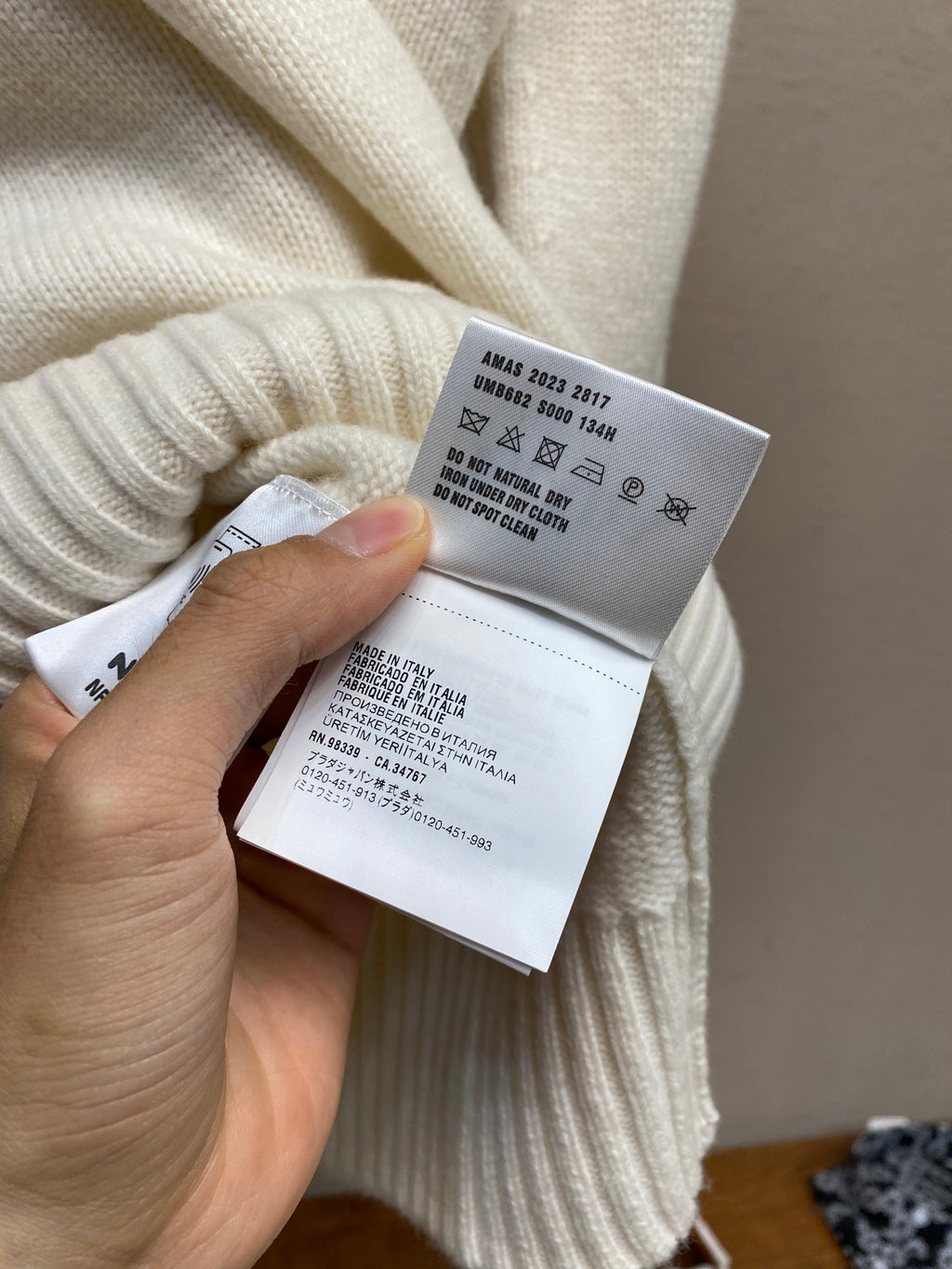Cream sweater care label attached at inside collar, with size and fabric details