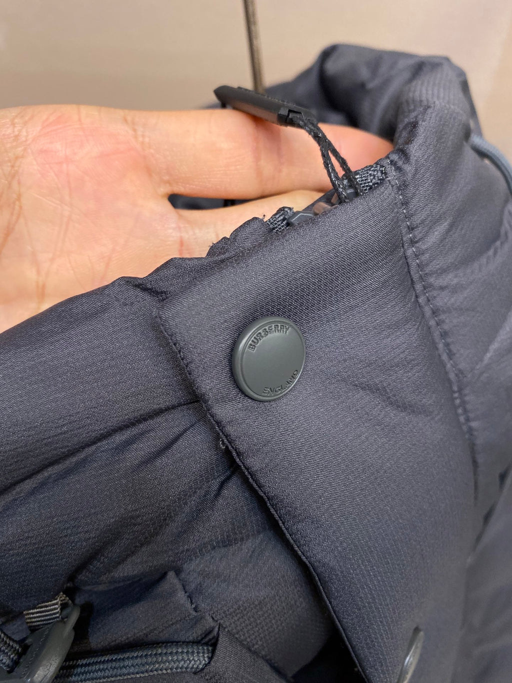 Dark gray puffer jacket cuff with round snap button and logo patch