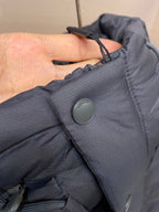 Dark gray puffer jacket cuff with round snap button and logo patch