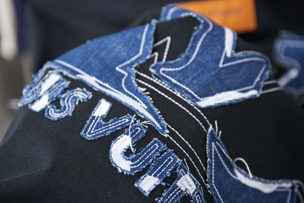 Close-up of blue embroidered LV-style lettering and monogram on dark fabric