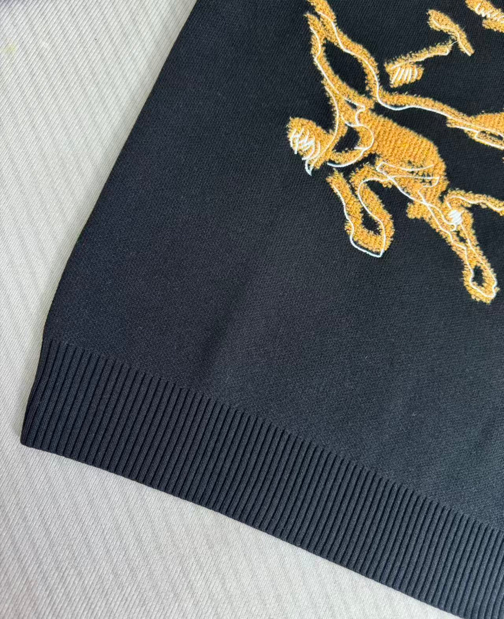 Navy sweater sleeve with gold horse crest embroidery detail
