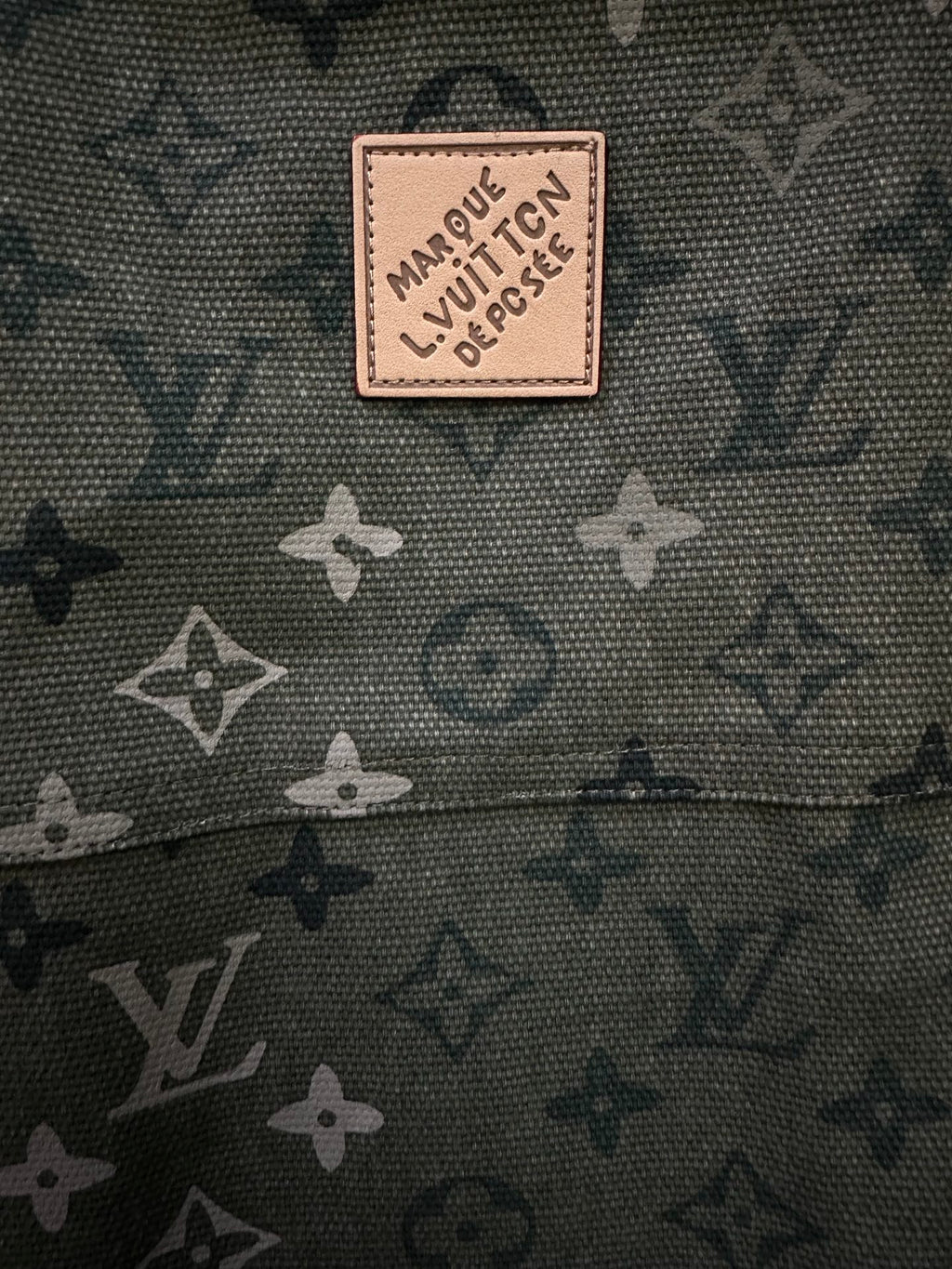 Beige logo patch on olive green monogram fabric.