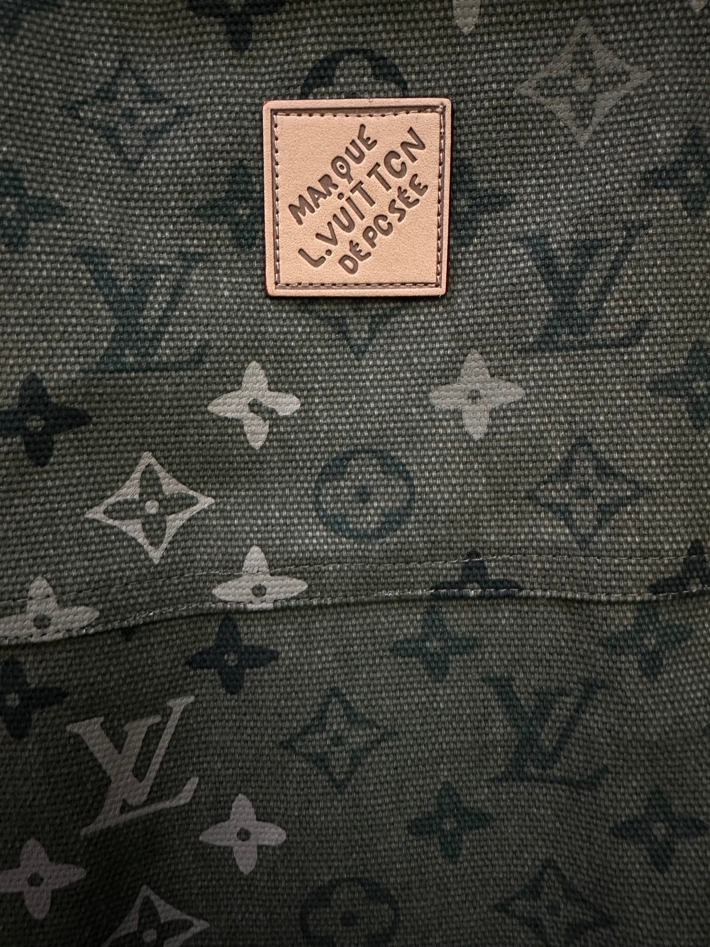 Beige logo patch on olive green monogram fabric.
