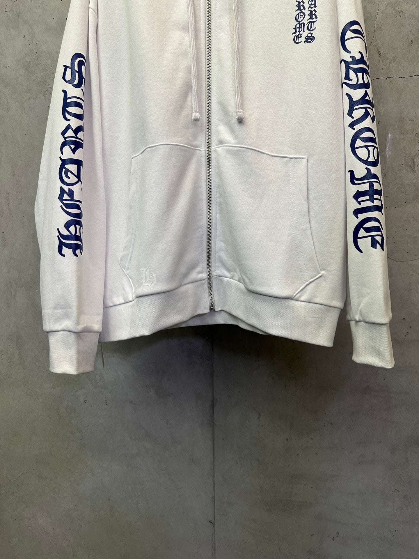 White zip-up hoodie front with kangaroo pocket and blue sleeve text accents