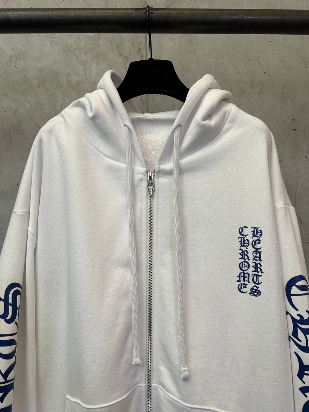 White zip-up hoodie close-up with silver zipper and chest logo text print