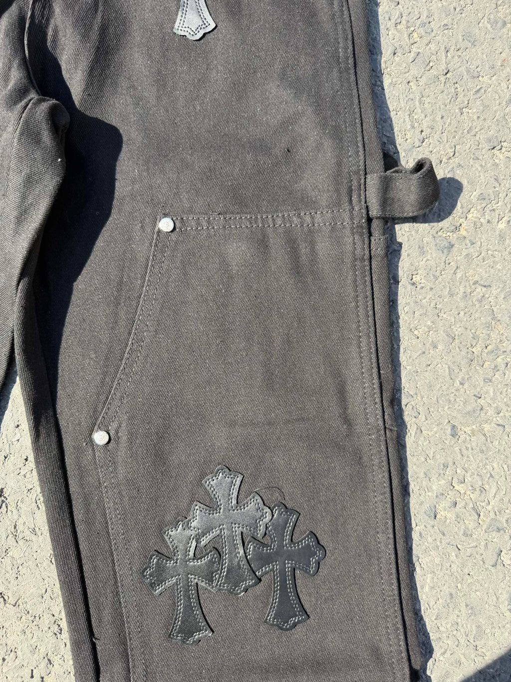 Black cargo pants leg close-up with cross patch and side pocket button