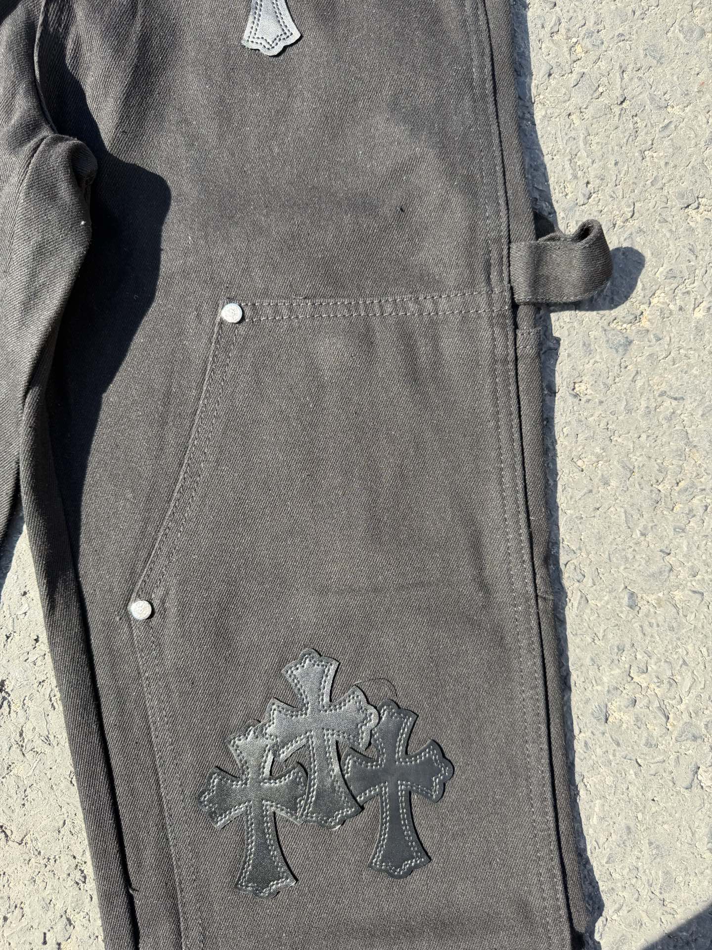 Black cargo pants leg close-up with cross patch and side pocket button