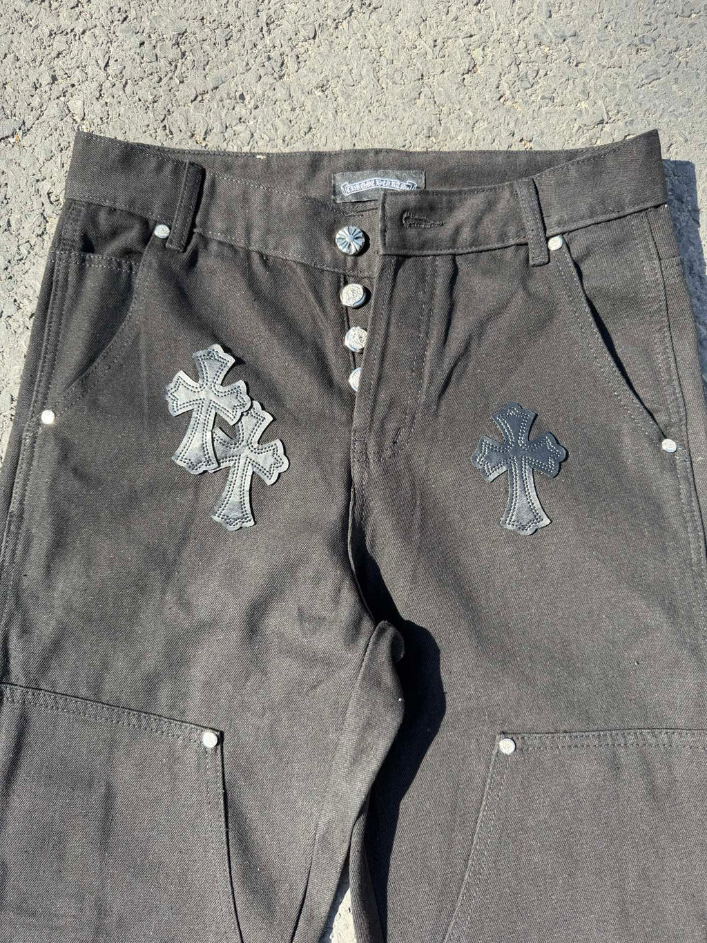 Black cargo pants close-up with front buttons, drawstring cord, and cross embroidery