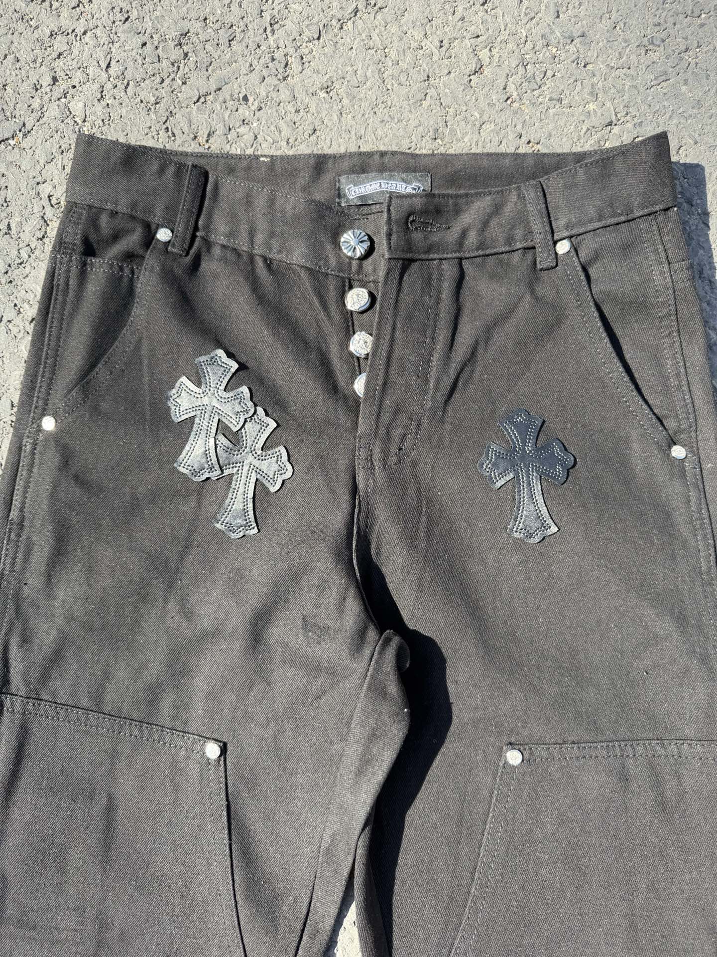Black cargo pants close-up with front buttons, drawstring cord, and cross embroidery