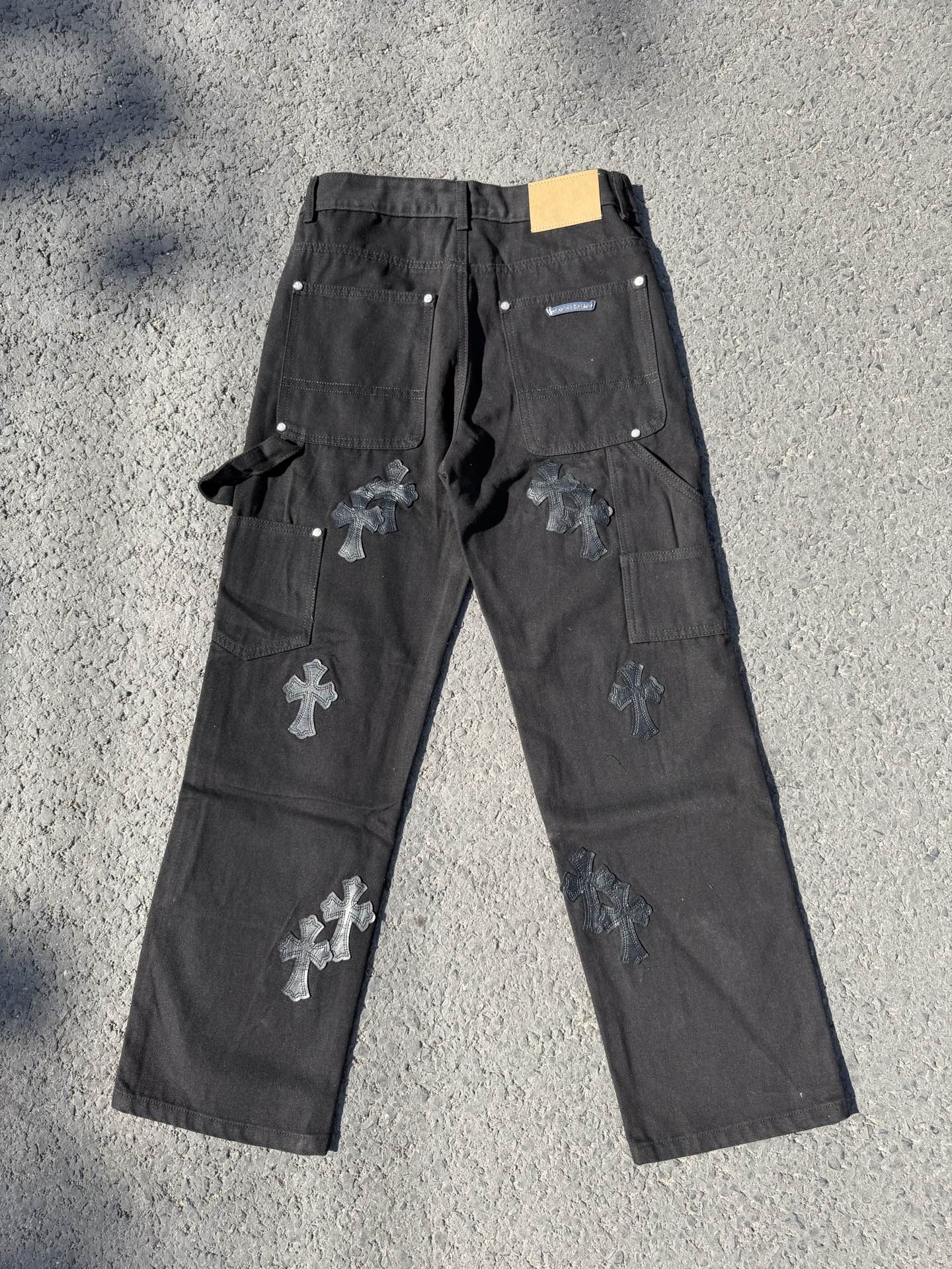 Black cargo pants with cross patches, drawstring tie, and small label at waistband