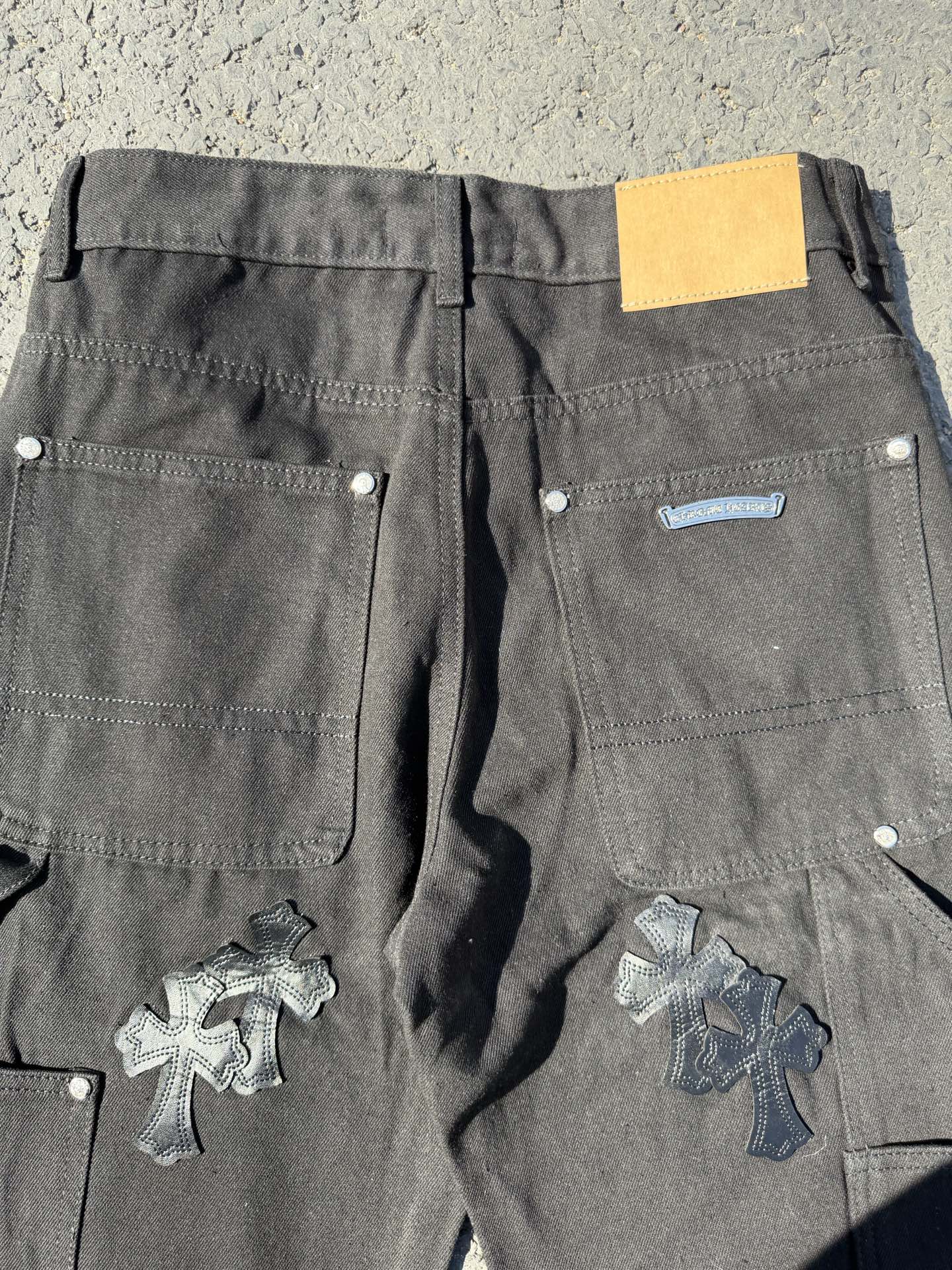 Black cargo pants with back pockets and cross patches, yellow label on waistband