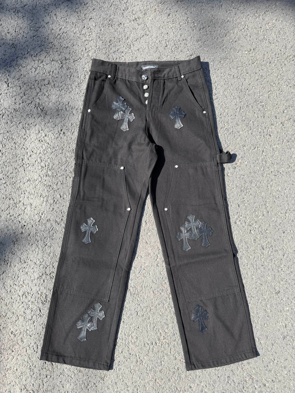 Black cargo pants with embroidered cross patches and metal snap buttons at waistband