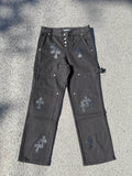 Black cargo pants with embroidered cross patches and metal snap buttons at waistband