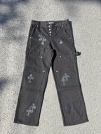 Black cargo pants with embroidered cross patches and metal snap buttons at waistband