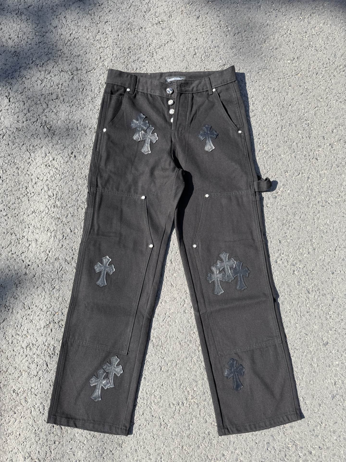 Black cargo pants with embroidered cross patches and metal snap buttons at waistband