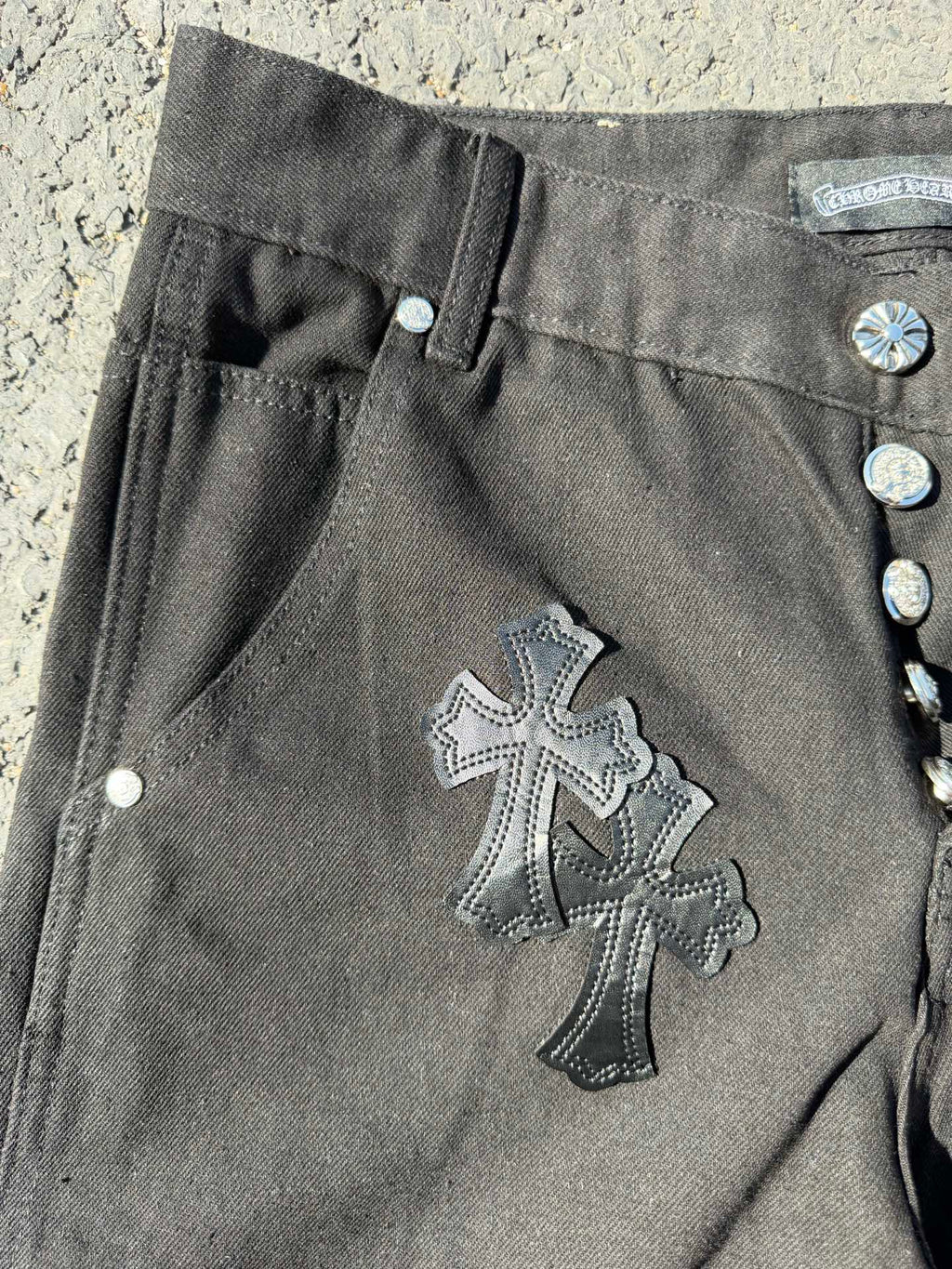 Black cargo pants detail with buttoned side pocket and large cross patch on leg