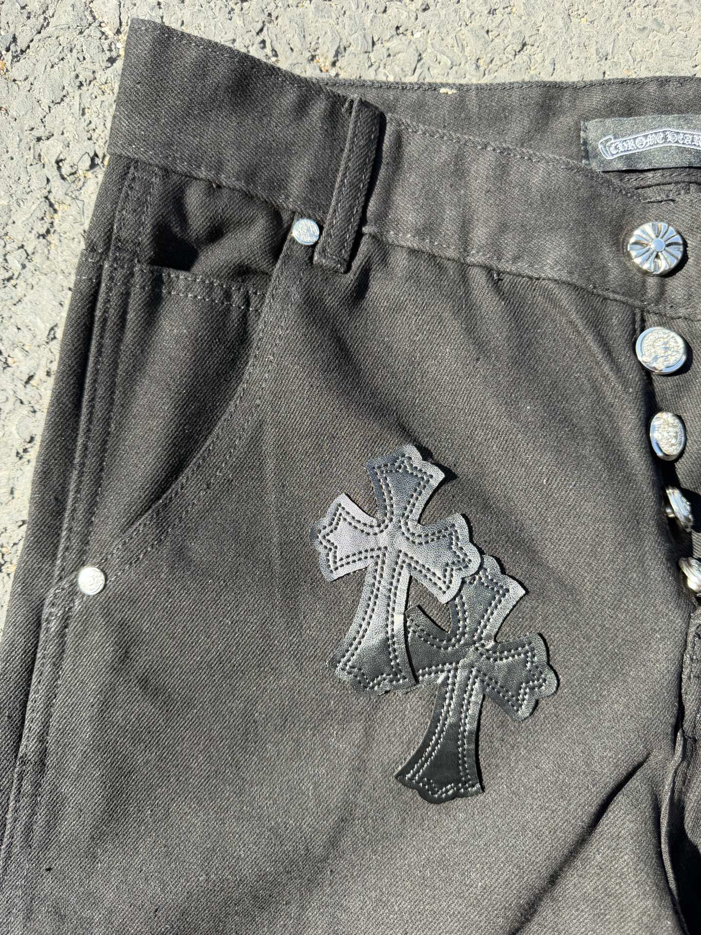 Black cargo pants detail with buttoned side pocket and large cross patch on leg