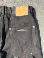 Black cargo pants with back pocket, metal button, and small cross patch near hem