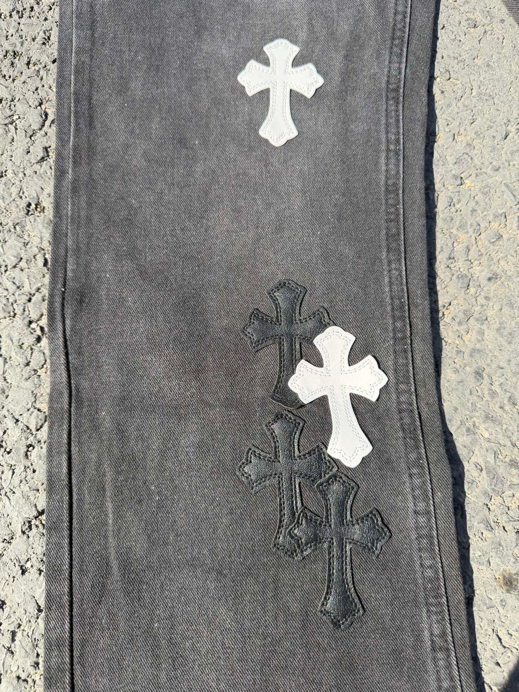 Close-up of dark gray denim pant leg with stacked cross patches in white and dark