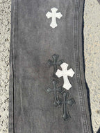 Close-up of dark gray denim pant leg with stacked cross patches in white and dark