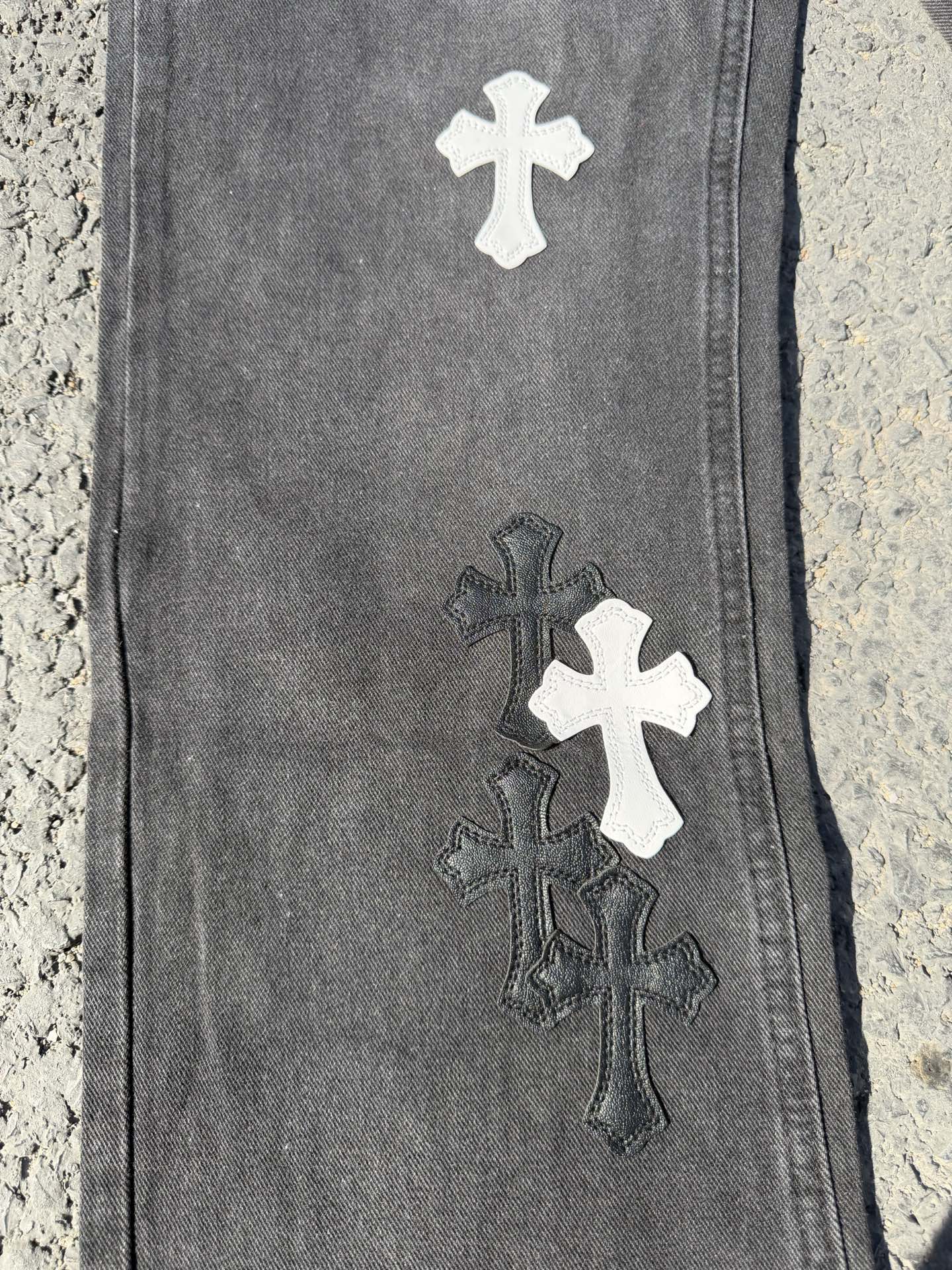 Close-up of dark gray denim pant leg with stacked cross patches in white and dark