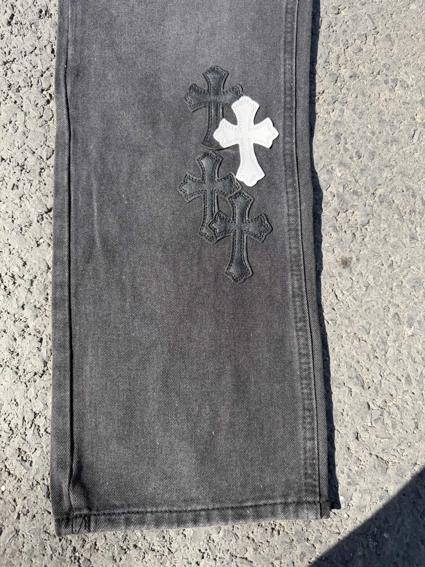 Dark gray jeans pants with dark cross patch near hem