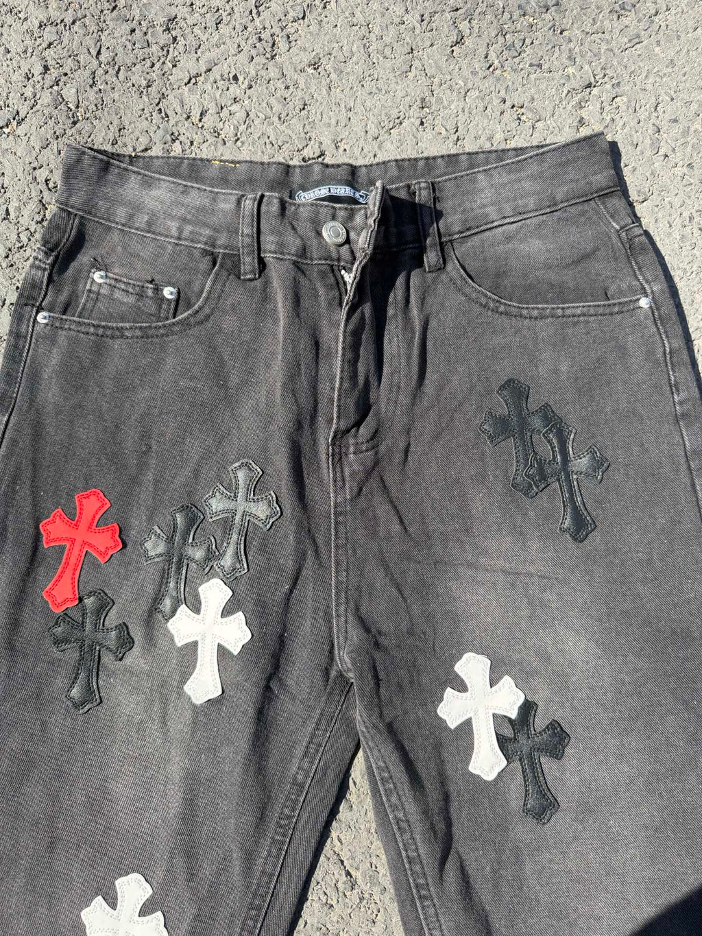 Close-up of dark gray denim pants with front button and cross patches on legs