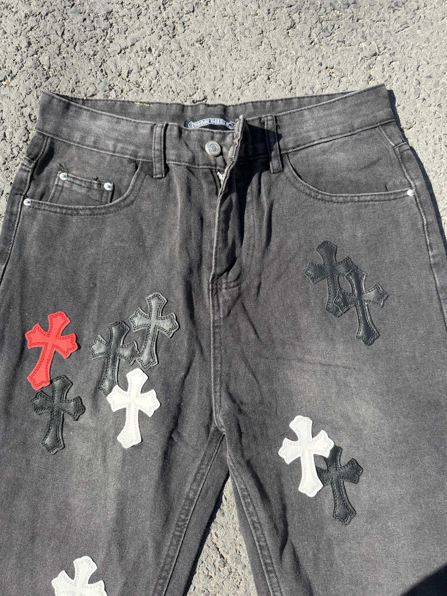 Close-up of dark gray denim pants with front button and cross patches on legs