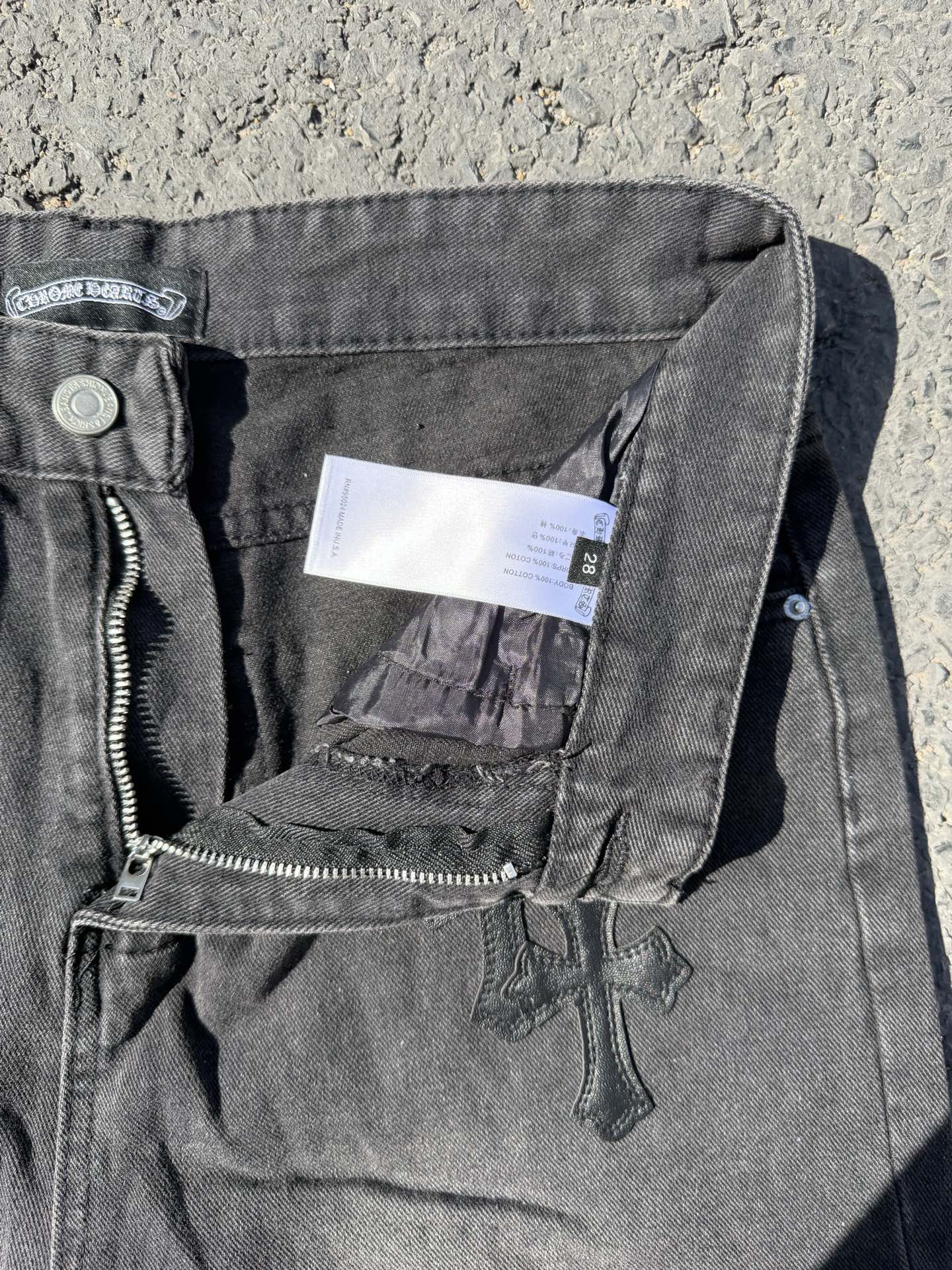 Dark gray denim pants showing front pocket, zipper fly, and small cross patch