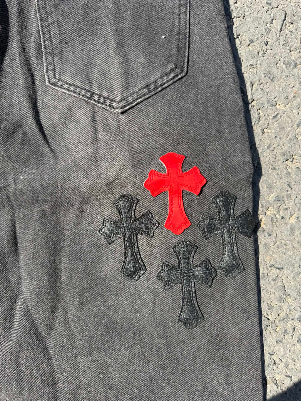 Close-up of dark gray denim pants with red cross and dark cross patch design
