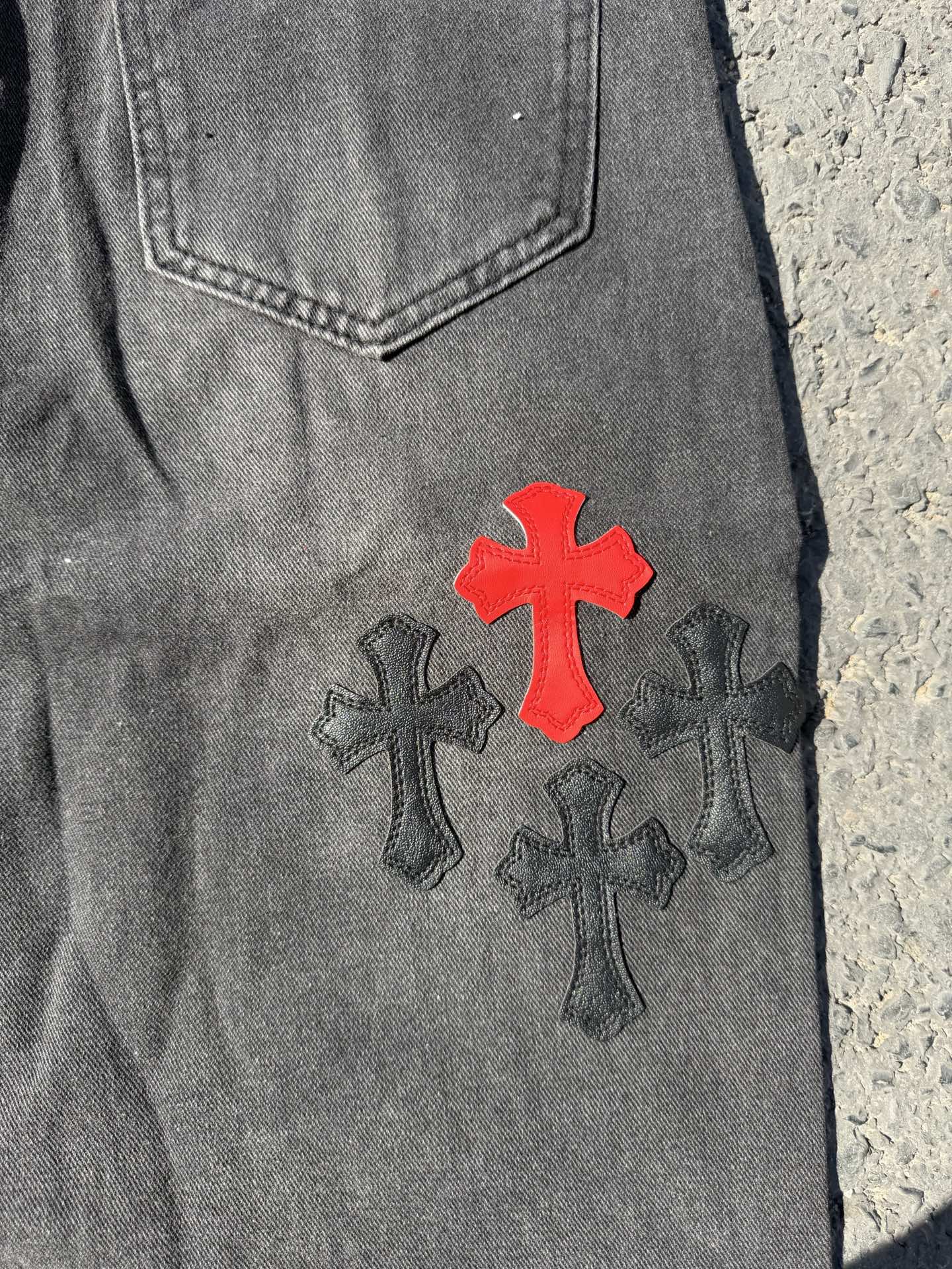 Close-up of dark gray denim pants with red cross and dark cross patch design
