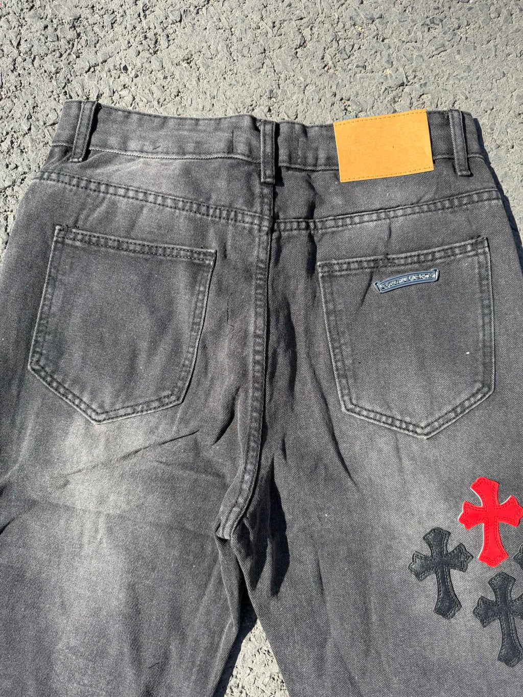 Dark gray denim pants with rear pockets and small cross patch on the right leg