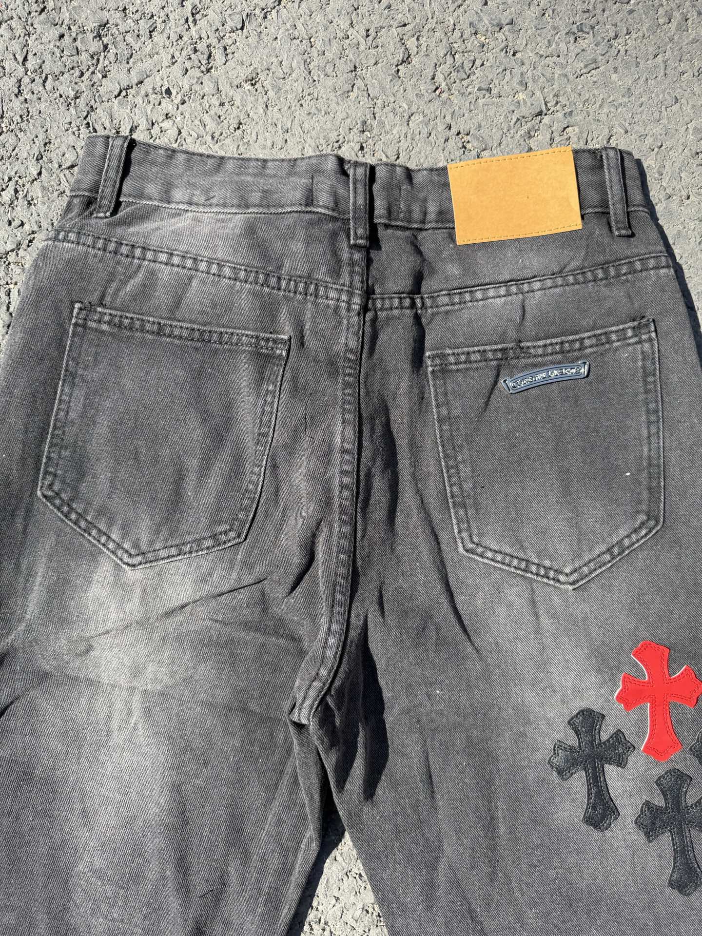 Dark gray denim pants with rear pockets and small cross patch on the right leg
