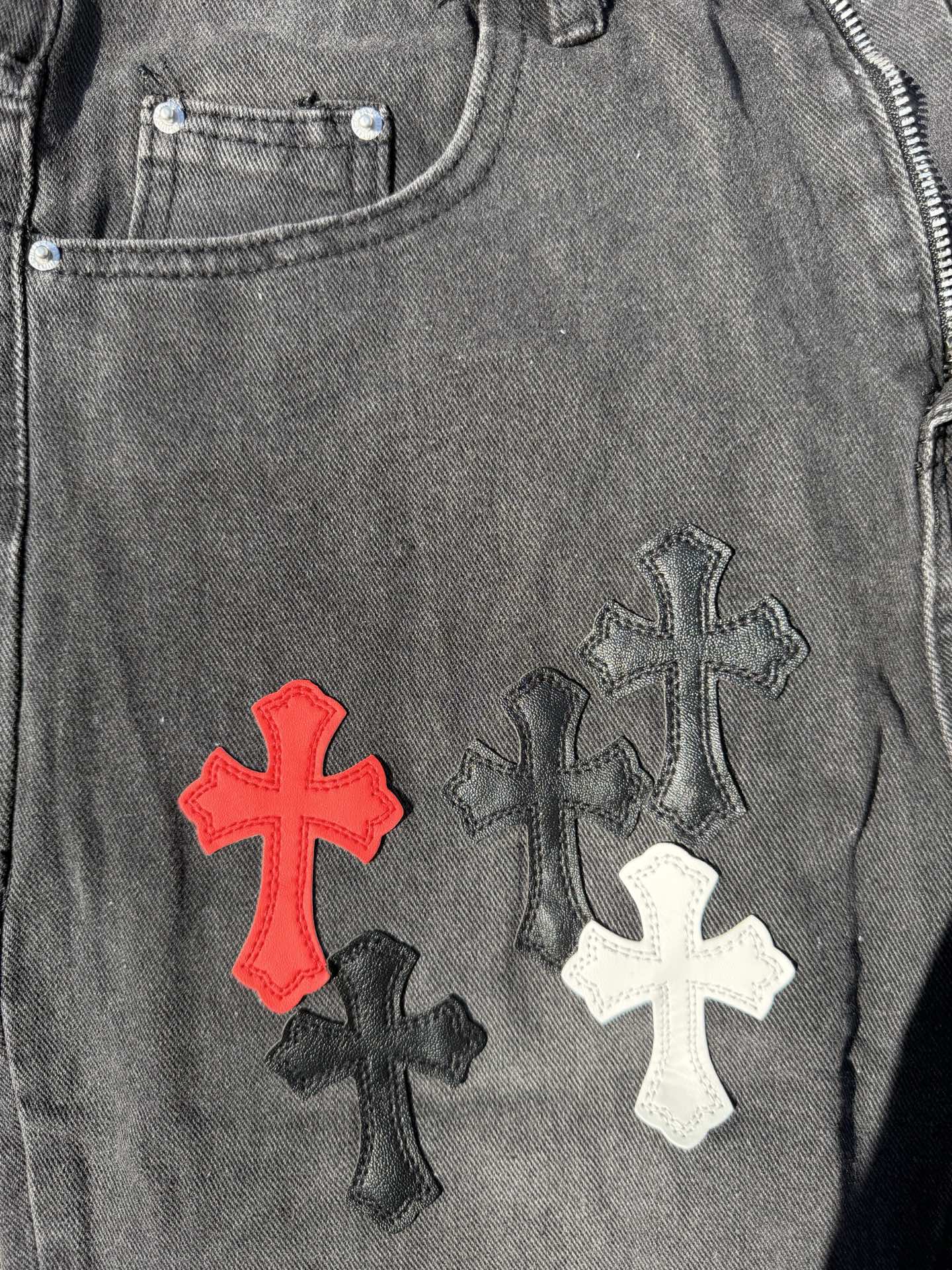 Close-up of dark gray denim pants with red, white, and black cross embroidery