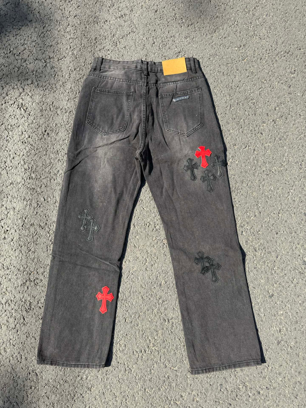 Dark gray denim pants with scattered cross patches in red and white on the front
