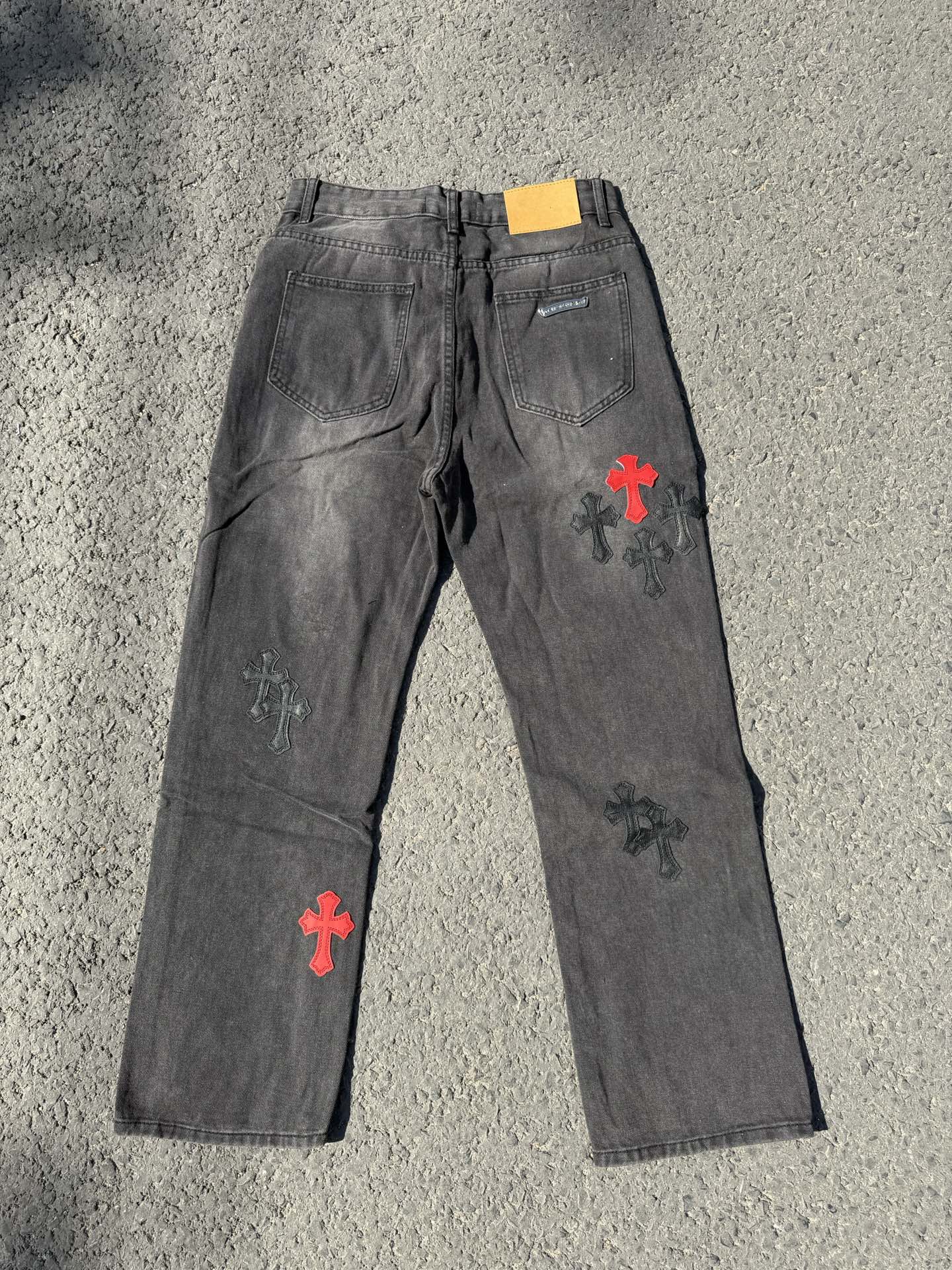 Dark gray denim pants with scattered cross patches in red and white on the front